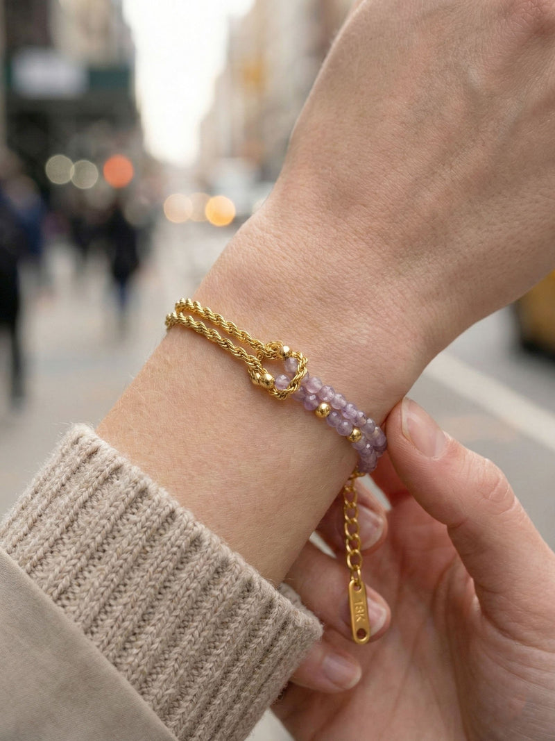 Armband Twist Violetta am Handgelenk getragen – Nahaufnahme der violetten Amethyst-Perlen und goldenen Knotenverschlingung