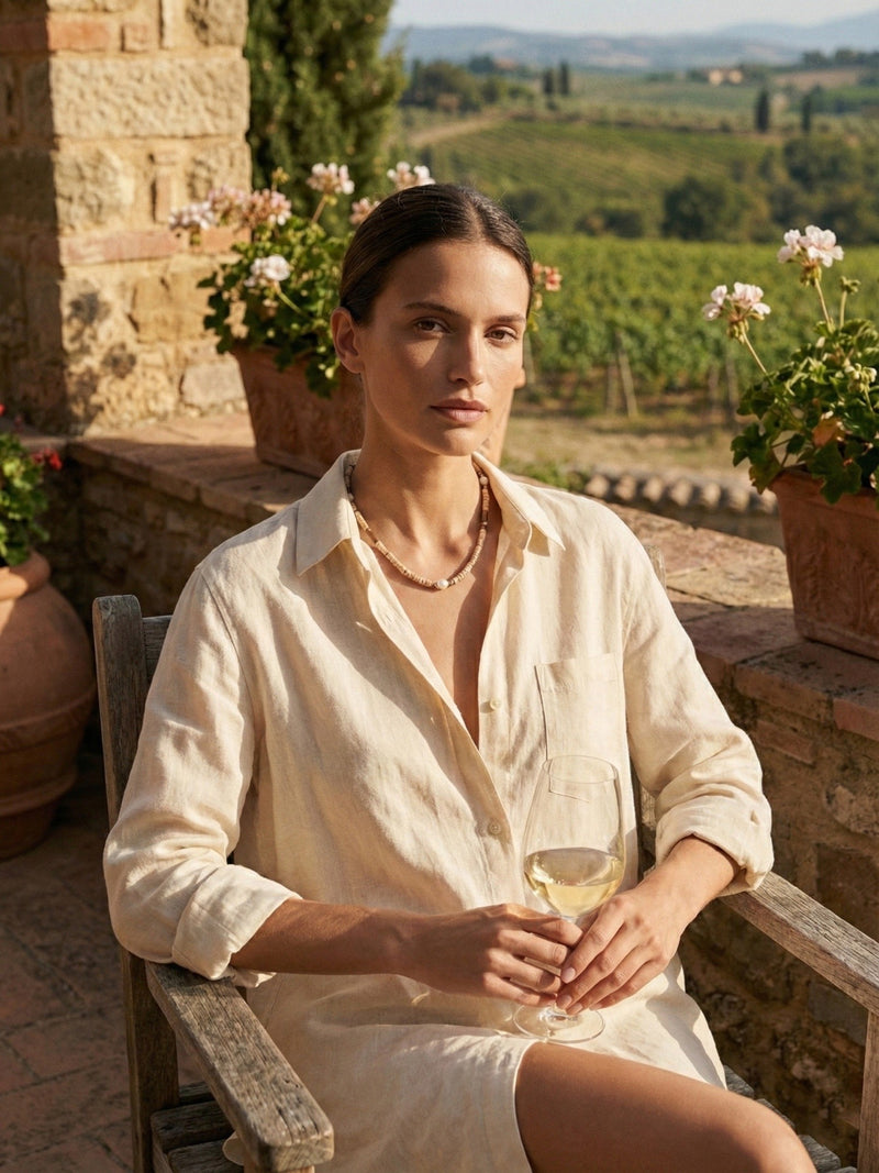 Earthlines Kette Toskana Lifestyle – Frau in beigem Leinenhemd auf toskanischer Terrasse mit Weinglas Weinberg-Panorama