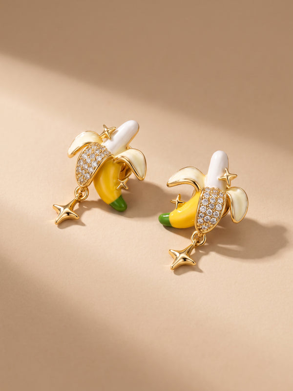 EH54: Bananen-Ohrringe mit hellen Schalen, gelben Details und Sternanhängern auf beigefarbenem Untergrund.