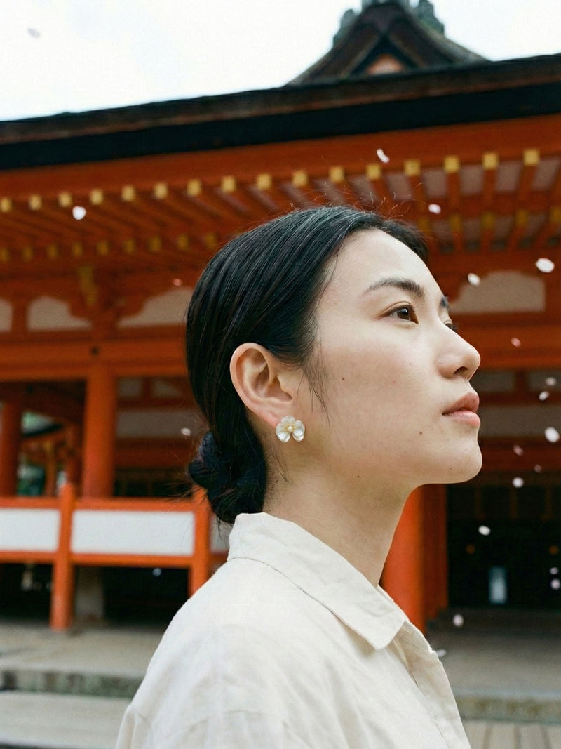 Perlmuttbluete Ohrringe getragen – Model traegt Blumen-Ohrstecker vor japanischem Tempel mit Kirschblueten