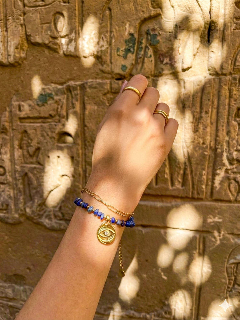 Schutzblick Armband Hand Hieroglyphen – Vergoldetes Lapislazuli-Armband am Handgelenk vor aegyptischer Steinwand Sonnenlicht