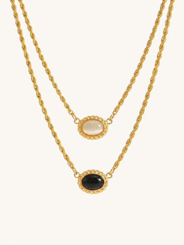 Yin Yang Glow Kette Produktfoto – vergoldete Doppelkette mit hellem und dunklem Katzenauge-Stein auf weissem Hintergrund