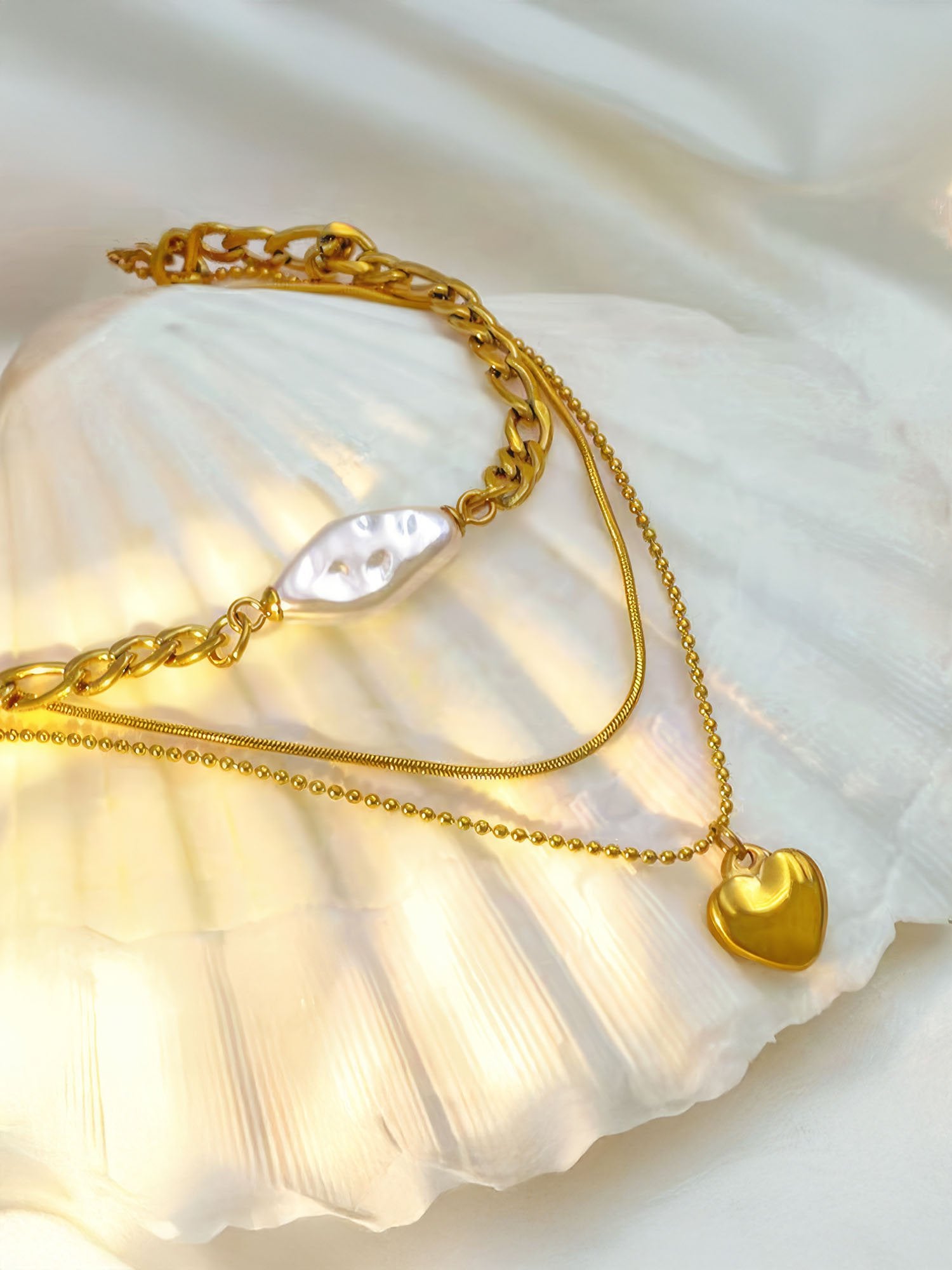 Dreireihige Goldkette Herzstück auf Muschel drapiert - Vergoldete Layering-Halskette mit Perle und Herz-Anhänger in maritimer Inszenierung