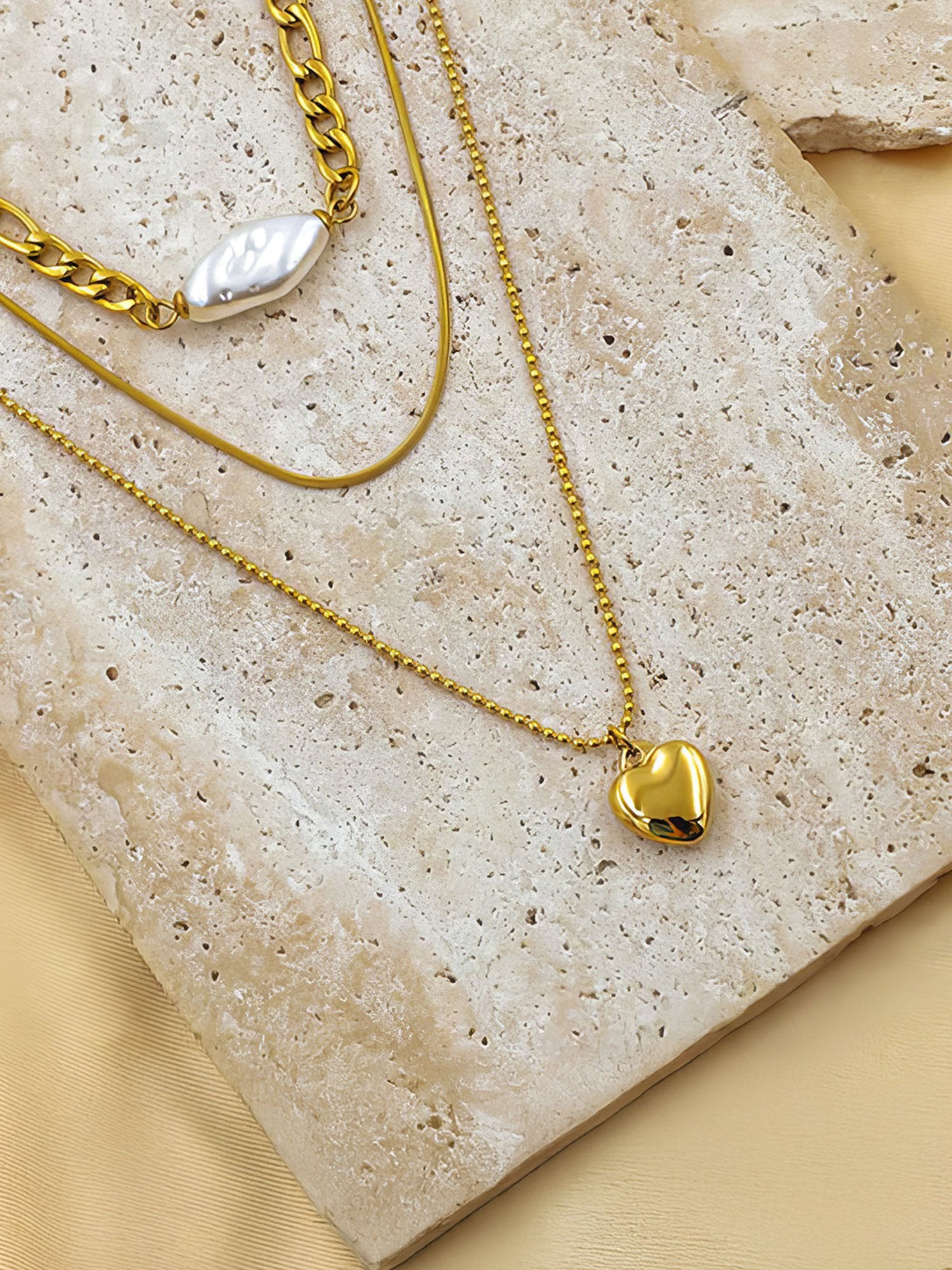 Goldene Layering-Kette mit Herz auf Steinplatte - 18K vergoldete dreireihige Halskette mit Perlenelement Flatlay-Fotografie