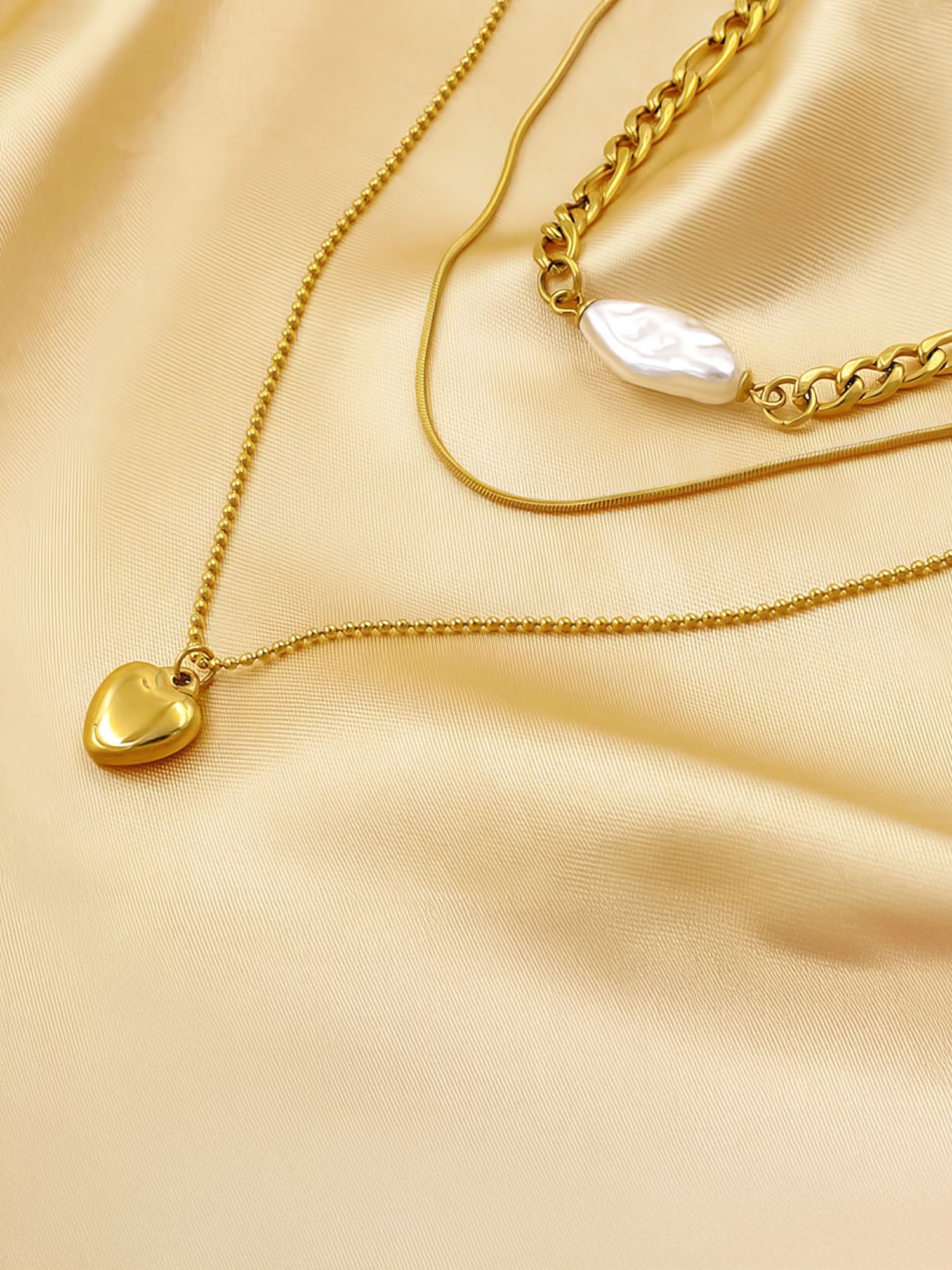 Herzstück Layering-Kette auf goldenem Satin - Dreifach-Halskette mit Herzanhänger und Perle in warmer Stoffinszenierung