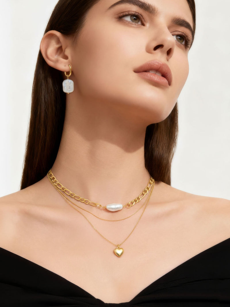 3er-Kette Herzstück Tragedetail – Goldene Layering-Halskette mit Herzanhänger Nahaufnahme am Dekolleté schwarzes Oberteil