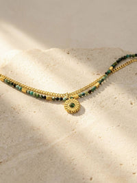 Afrikanischer Turkis Perlenarmband auf hellem Steinuntergrund - Zweireihiges Boho Armband mit Goldkette im Sonnenlicht