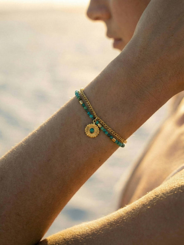 Boho Turkis Armband im goldenen Sonnenuntergangslicht getragen - Edelstein Handschmuck mit Sonnenblumen Anhaenger am Strand