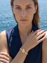 Armband Benedizione am Meer – Model im dunkelblauen Top zeigt Kristallarmband mit Guadalupe-Medaillon, tuerkisblaues Wasser im Hintergrund