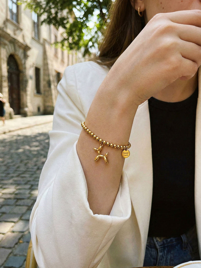 Armband Glueckshund am Handgelenk getragen – goldene Perlen und verspielter Ballonhund-Charm am Arm
