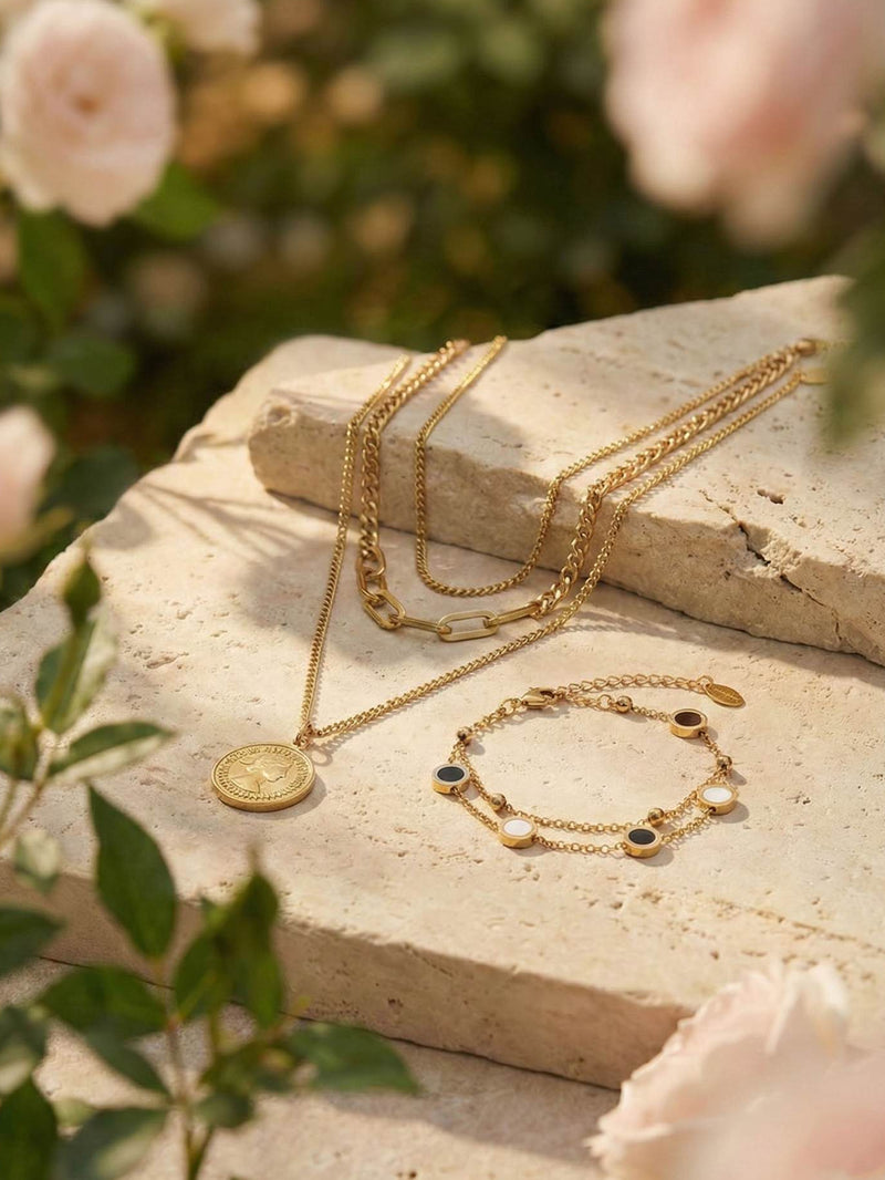Goldenes Luna Dual Emaille-Armband mit Muenzkette vor unscharfem Rosenhintergrund - luxurioese Schmuckfotografie