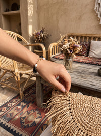 Armband Midnight Pearl am Handgelenk neben einer geflochtenen Tasche im Café