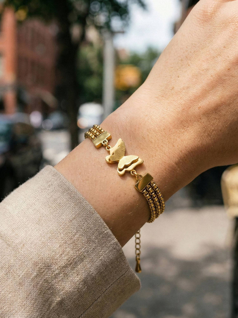 Armband Papillon am Handgelenk – Nahaufnahme des goldenen Schmetterlings mit texturierten Fluegeln und dreifacher Kette