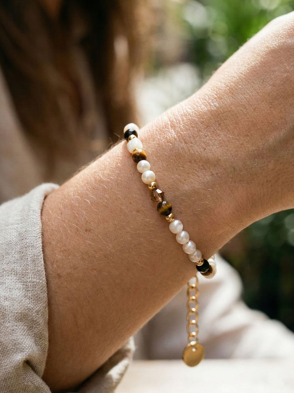 Armband Sahel am Handgelenk getragen – cremefarbene Muscheln und braune Tigerauge-Perlen im Sonnenlicht