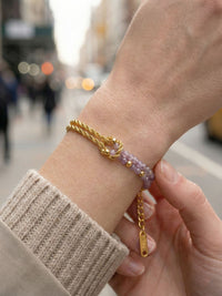 Armband Twist Violetta am Handgelenk getragen – Nahaufnahme der violetten Amethyst-Perlen und goldenen Knotenverschlingung