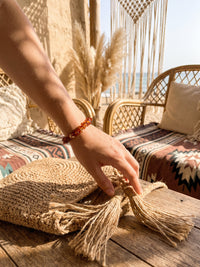 Armband Vulkanblüte am Handgelenk neben einer Strohtasche und hellen Textilien