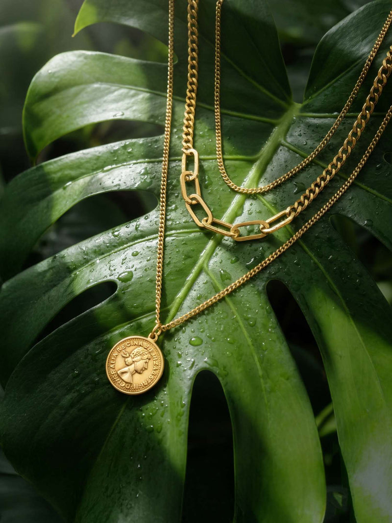 Aurelia Münzkette tropisches Flatlay - Goldene Layering-Kette auf Monstera-Blatt mit Wassertropfen frisches Naturdesign