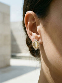 Celestia Ohrringe Detail-Nahaufnahme am Ohr – funkelnde Zirkonia-Steine und Katzenauge-Cabochon in goldener Fassung