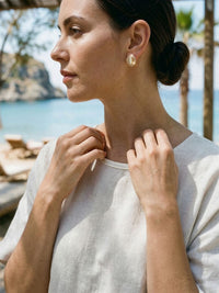 Celestia Ohrringe Kuesten-Lifestyle – Model mit Katzenauge-Ohrsteckern am Strand, entspannte Sommeratmosphaere mit Meerblick