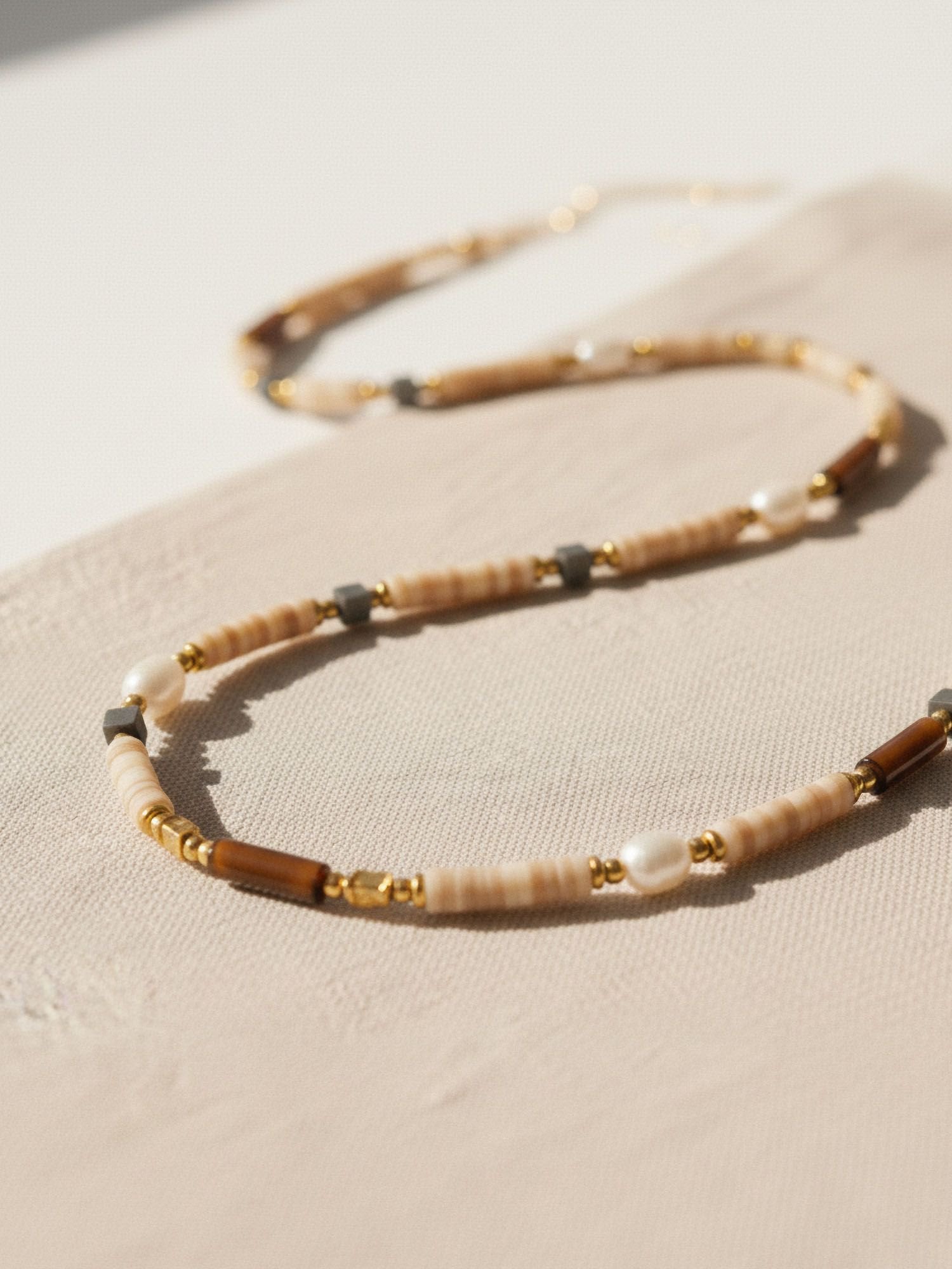 Earthlines Boho-Halskette Flatlay - Perlenkette mit warmem Farbverlauf aus Natursteinen und Süßwasserperlen auf hellem Hintergrund