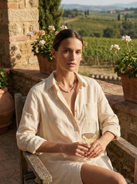 Earthlines Kette Toskana Lifestyle – Frau in beigem Leinenhemd auf toskanischer Terrasse mit Weinglas Weinberg-Panorama