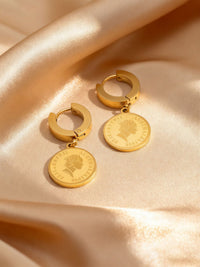 Queens Coin Ohrringe Flatlay mit Licht und Schatten - Vergoldete Münz-Creolen auf beigem Satin elegant inszeniert