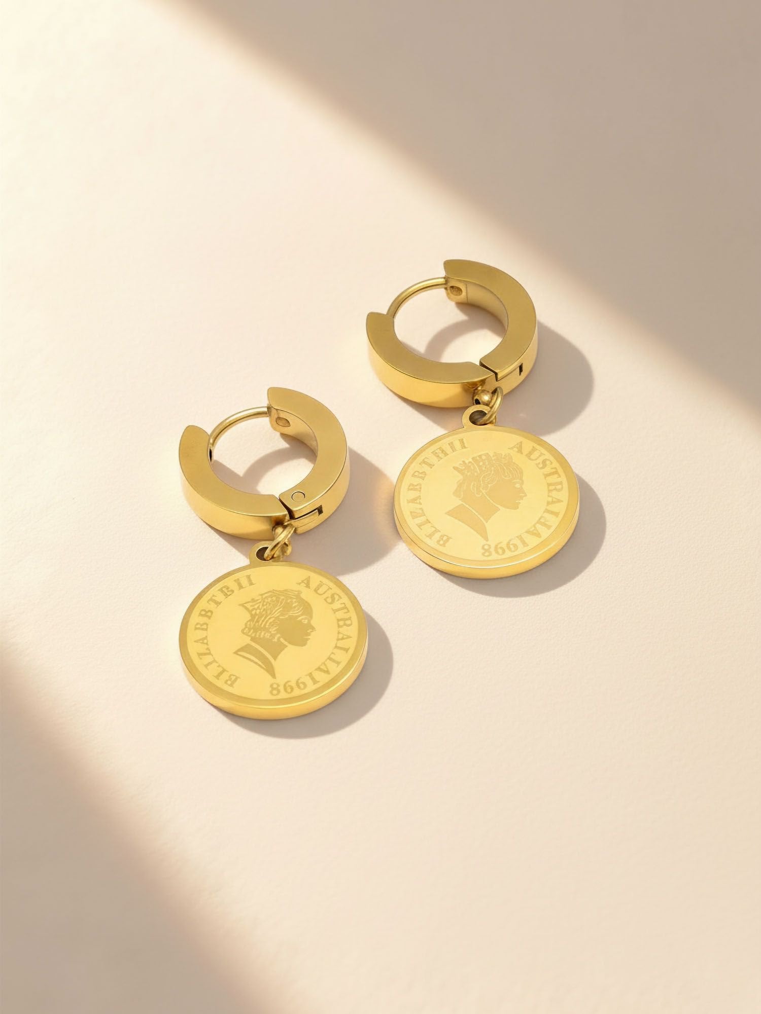 Queens Coin Ohrringe mit Schatten-Effekt - 18K vergoldete Münz-Creolen in warmem Licht Flatlay-Fotografie