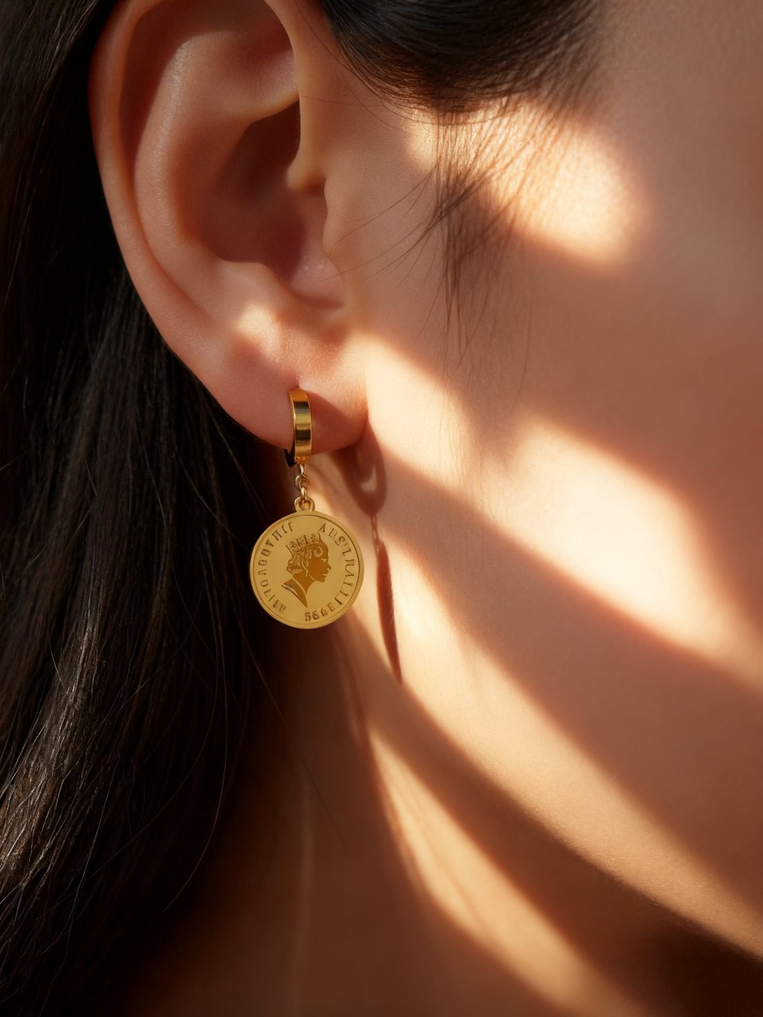Queens Coin Ohrringe getragen - Goldene Creolen mit Elizabeth II Münzanhänger am Ohr im natürlichen Sonnenlicht