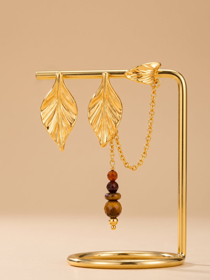 EH57: Asymmetrische goldfarbene Blatt-Ohrringe mit braunen Perlen, Verbindungskette und Ear-Cuff am Ständer.