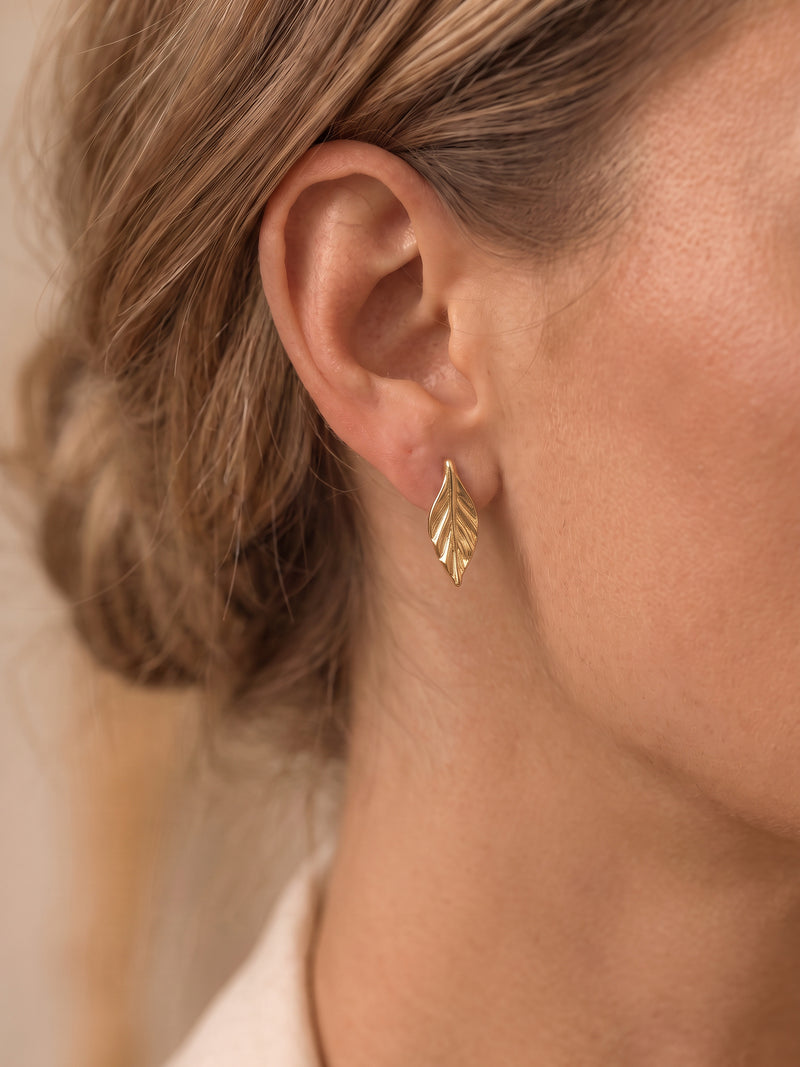 EH57: Schlichte Seite des asymmetrischen Paars mit goldfarbenem Blattstecker, am Ohr getragen.