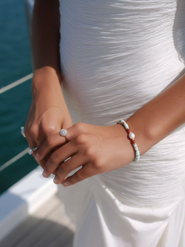 Sommerliches Lifestyle-Bild: Armband mit Shoushan-Stein und Perle am Handgelenk einer Frau im weißen Top auf einem Boot