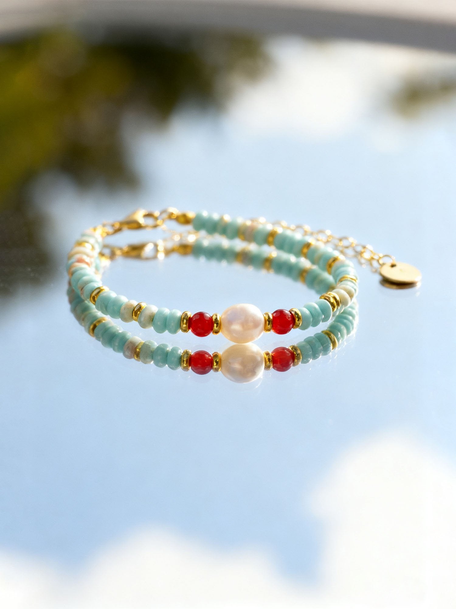 Doppelreihiges Perlenarmband Farbtupfer aus Fernost mit türkisen Glasperlen, rotem Shoushan-Stein und Süßwasserperle in goldener Fassung – Lifestyle-Aufnahme vor natürlichem Hintergrund