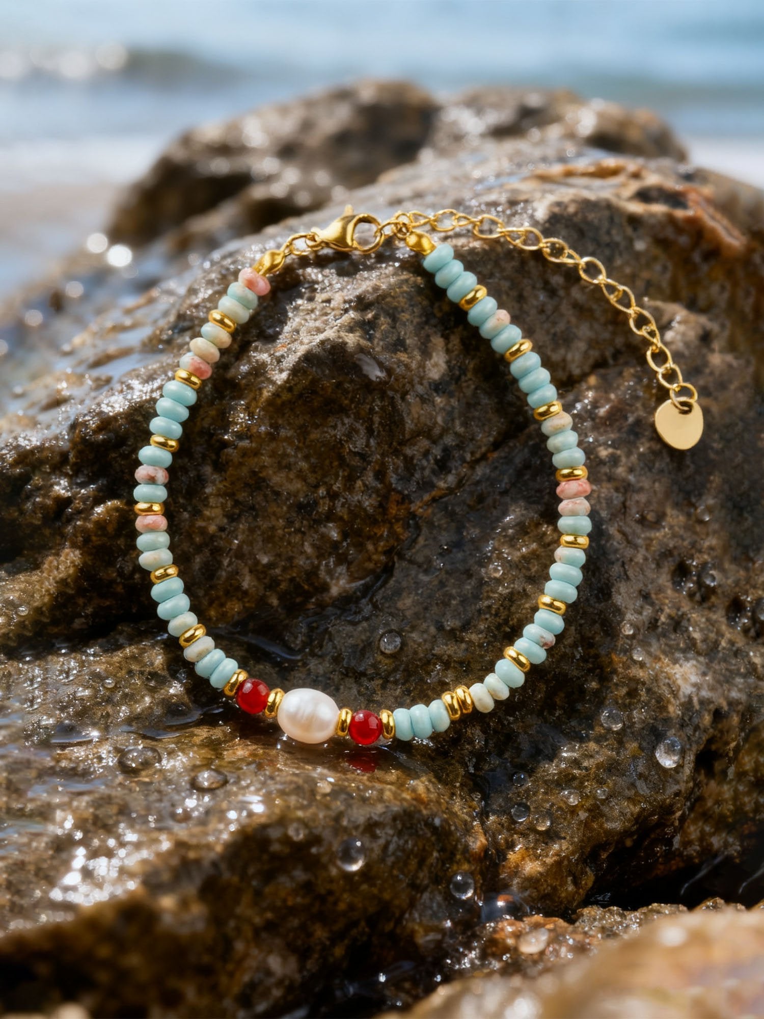 Asiatisch inspiriertes Armband auf nassem Felsen am Meer – detailreiche Nahaufnahme der türkisen Perlen, roten Shoushan-Steine und goldenen Zwischenperlen