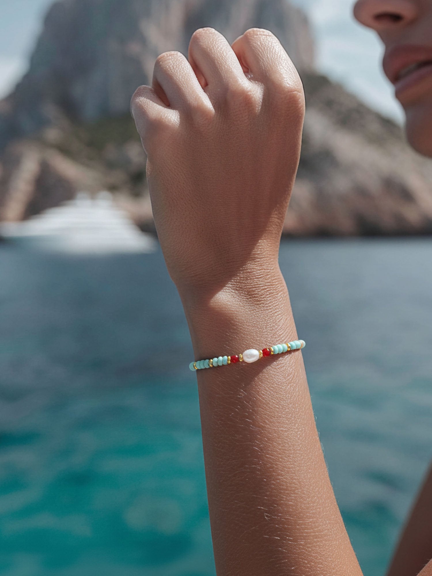 Frau trägt türkises Perlenarmband Farbtupfer aus Fernost am Handgelenk – natürliche Trageansicht vor Meeres-Kulisse