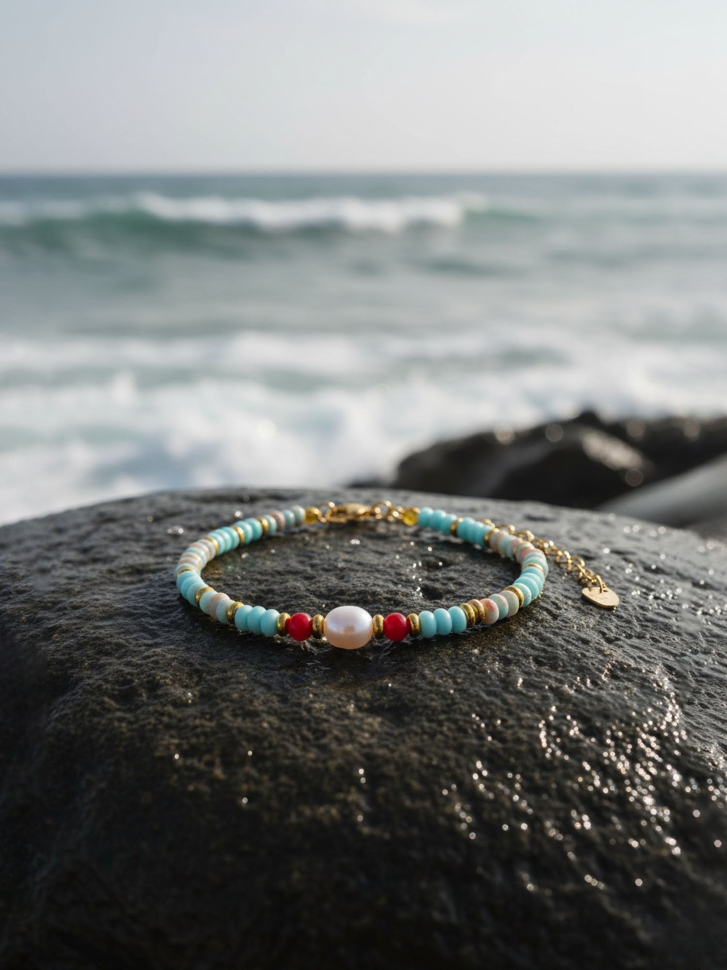 Elegantes Natursteinarmband auf dunklem Vulkangestein präsentiert – maritime Lifestyle-Fotografie mit verschwommenem Meereshintergrund