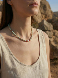 Model im Leinen-Top traegt Sommerglanz Kette vor Felskulisse Boho-Style Sommer-Accessoire natuerlicher Look