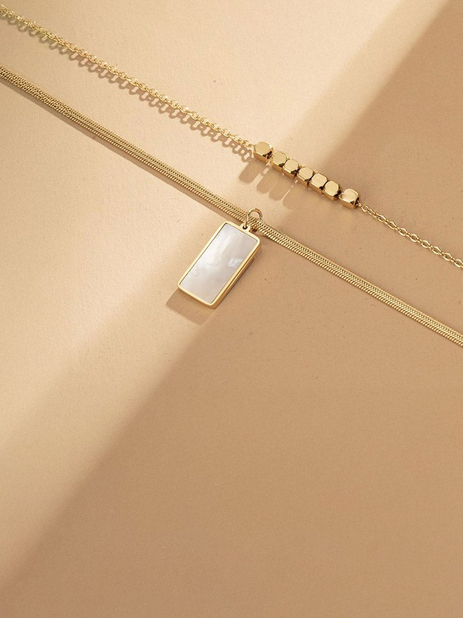 Detailansicht des Urban Mirror Spiegelanhängers – geometrischer Goldcham mit Perlenverzierung an feiner Kette