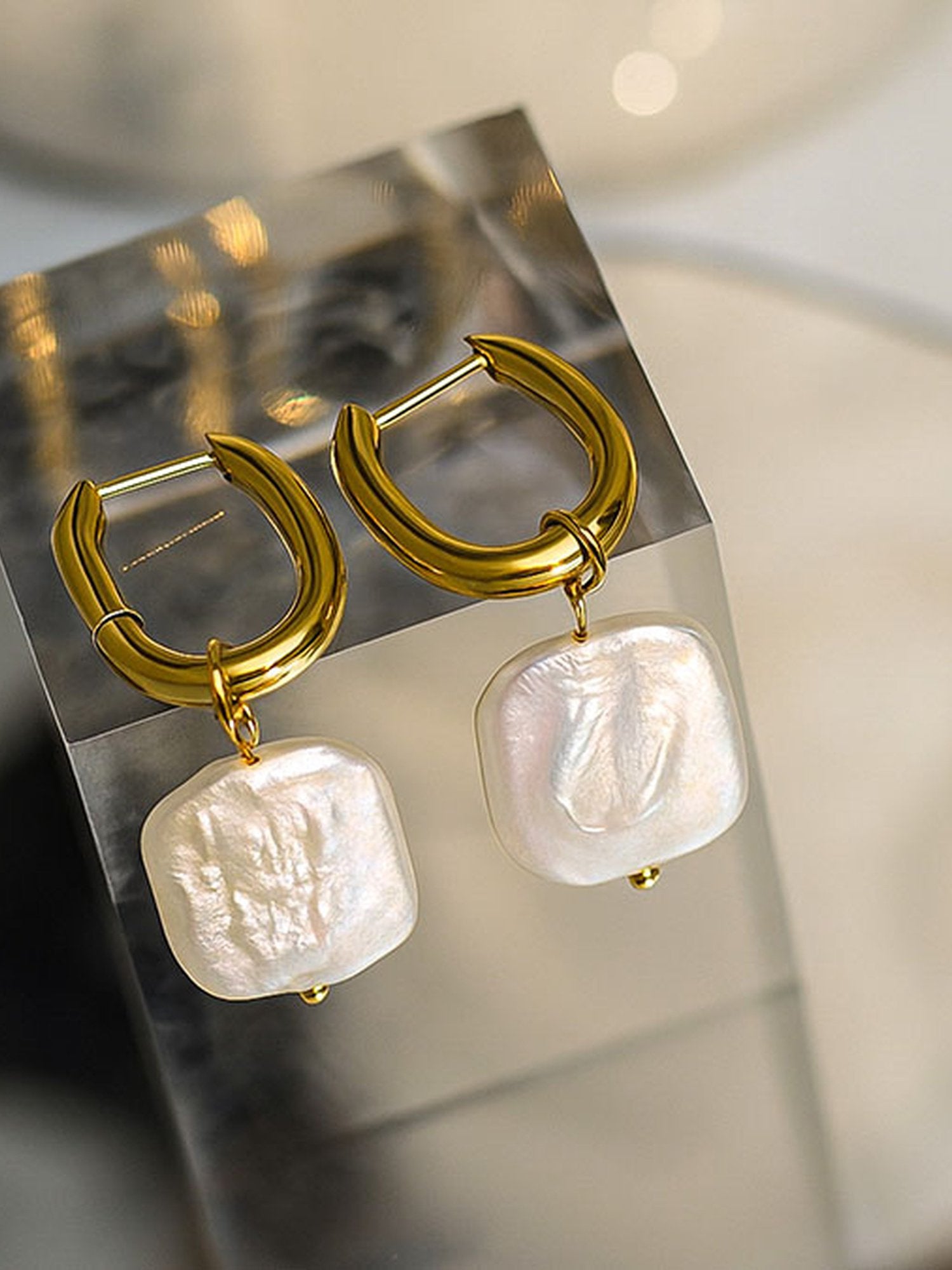 Marea Barock-Perlenohrringe Studio – organische Perlenform an goldenen U-Creolen auf weißem Grund