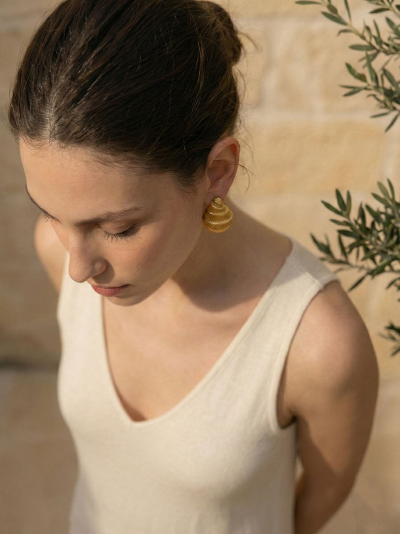 Golden Shell Ohrringe Model Portraet – Frau mit Hochsteckfrisur blickt nach unten, goldener Muschel-Ohrring sichtbar, Olivenzweig, sanftes Licht