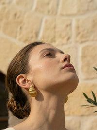 Golden Shell Ohrringe Profil – Model blickt nach oben im Sonnenlicht, vergoldeter Muschel-Ohrring am Ohr, mediterrane Atmosphaere