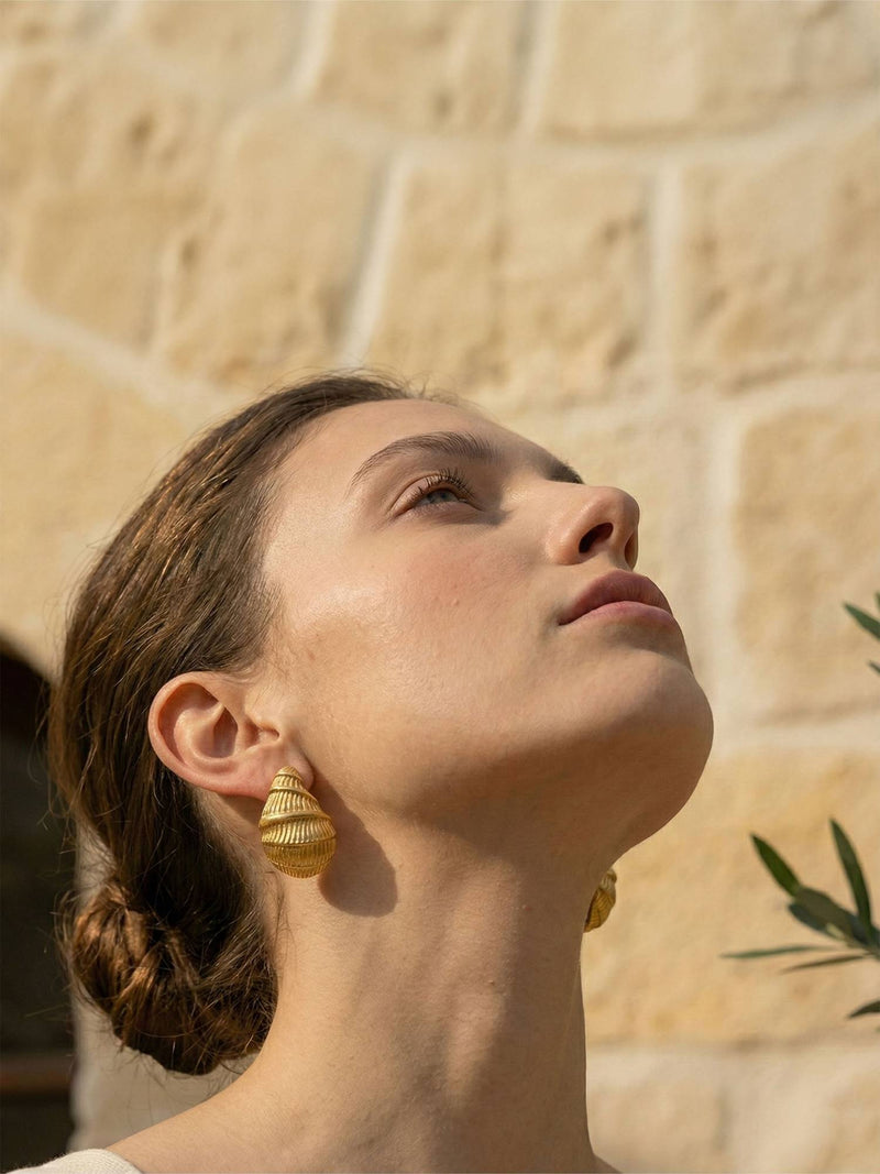 Golden Shell Ohrringe Profil – Model blickt nach oben im Sonnenlicht, vergoldeter Muschel-Ohrring am Ohr, mediterrane Atmosphaere