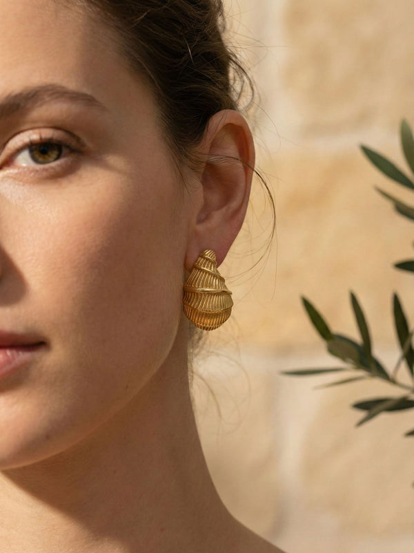 Golden Shell Ohrringe Nahaufnahme – halbes Gesicht mit goldenen Muschel-Ohrsteckern, gruen-braune Augen, Olivenzweig im Bild