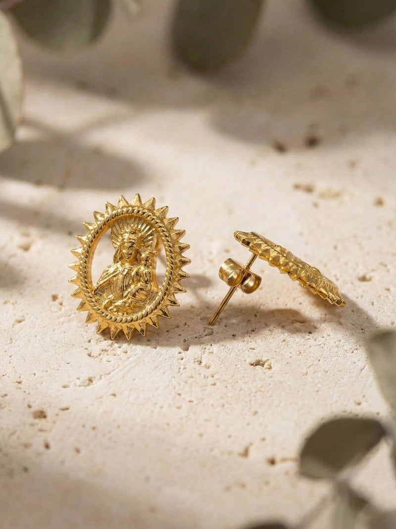 Gloria Ohrringe Flatlay – vergoldete Madonna-Ohrstecker auf Steinoberfläche mit Olivenzweig-Dekoration
