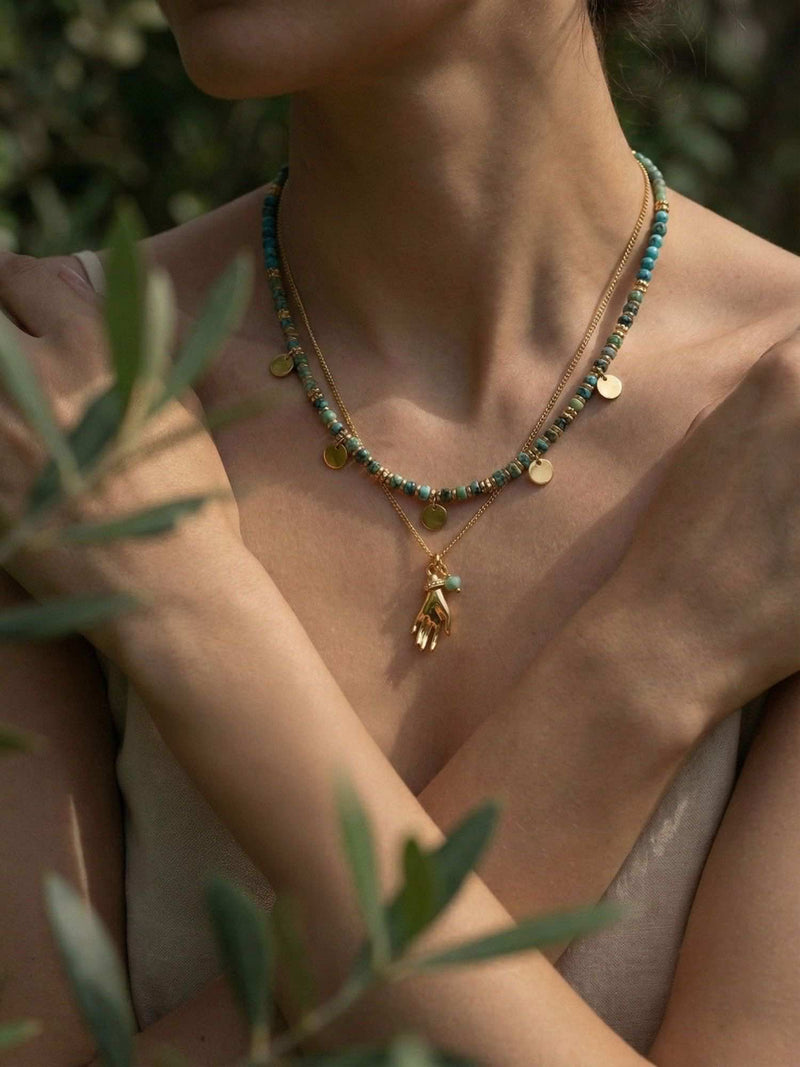 Model trägt Türkis Layering Ketten im Olivenhain - Nahaufnahme am Dekolleté mit goldenen Münzen und Hand-Anhänger im warmen Sonnenlicht