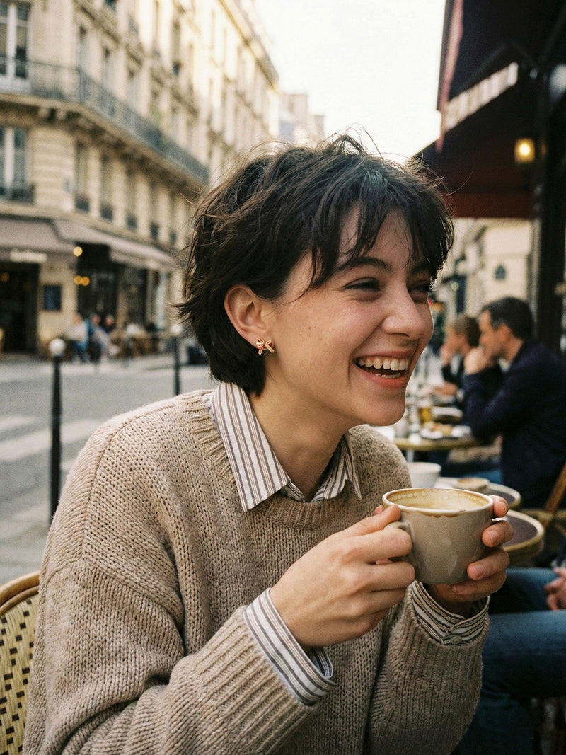 Schleife Kristall Ohrringe Lifestyle – junge Frau traegt vergoldete Schleifen-Ohrstecker im Pariser Cafe, romantischer Vintage-Stil