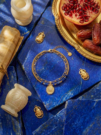 Schutzblick Armband Blau Flatlay – Lapislazuli-Armband auf blauem Stein mit aegyptischen Skarabaeus-Anhaengern Granatapfel orientalisch