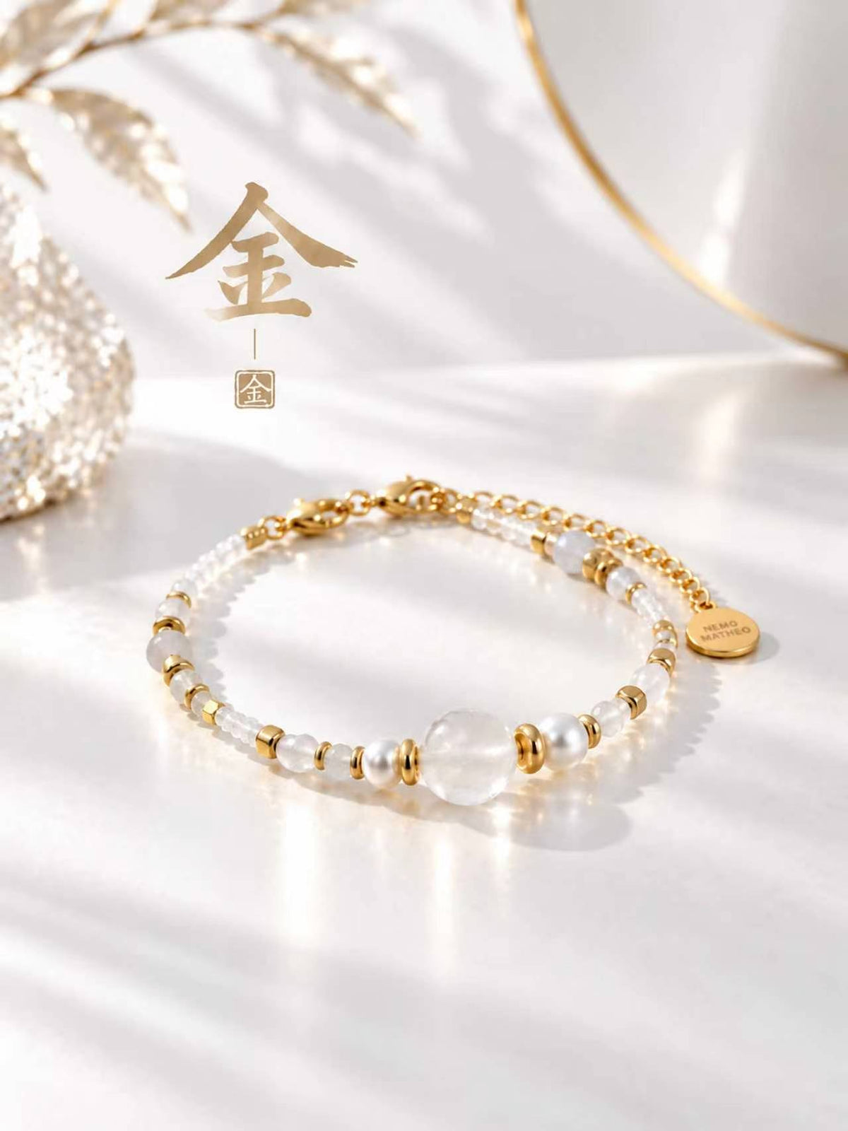 SL63A: Weißes Armband Cinque Elementi Metall mit goldfarbenen Details und dem chinesischen Zeichen 金 im Stillleben.
