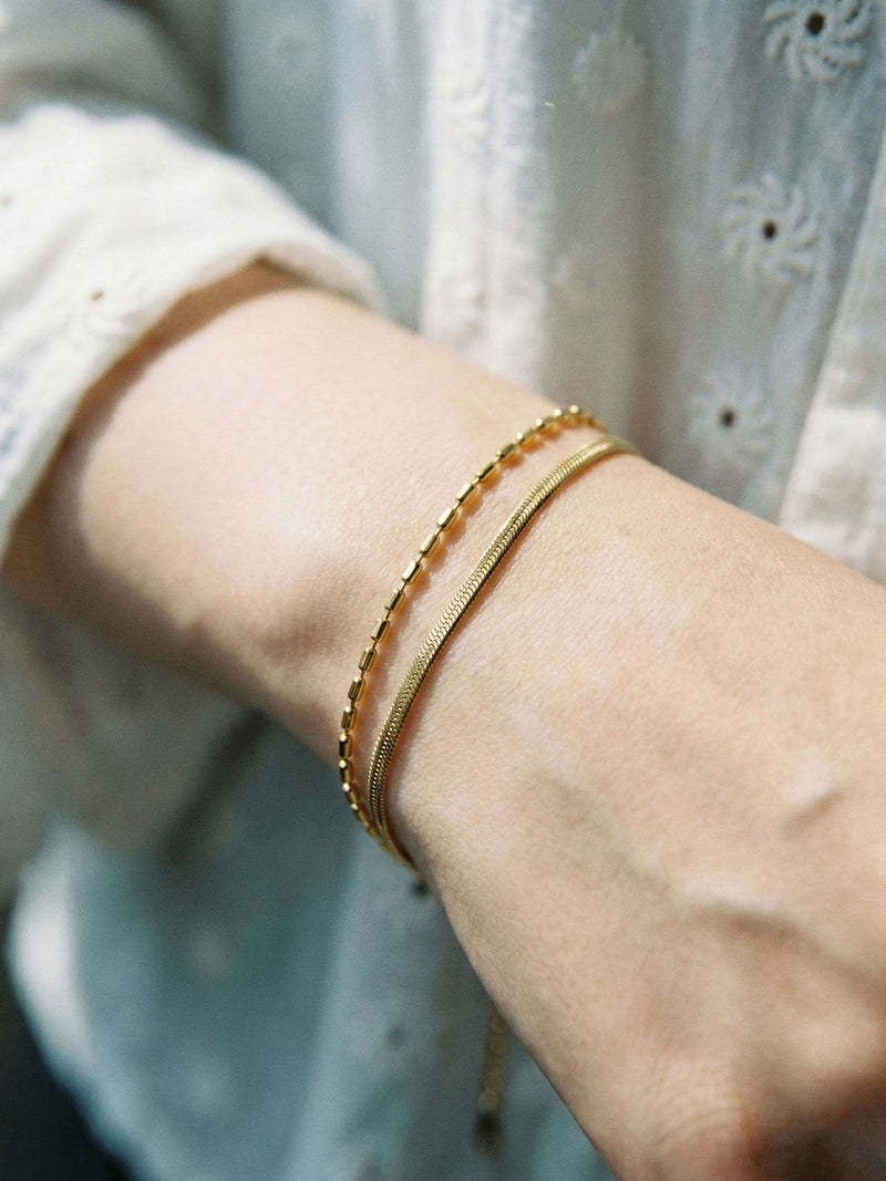 Snake and Bead Armband am Handgelenk getragen – goldene Schlangen- und Perlenkette im Sonnenlicht