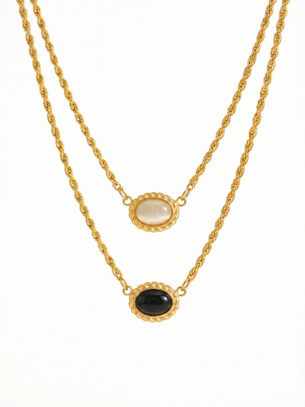 Yin Yang Glow Kette Produktfoto – vergoldete Doppelkette mit hellem und dunklem Katzenauge-Stein auf weissem Hintergrund
