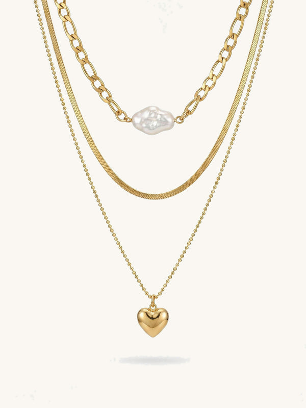 3-teilige goldene Halskette mit Herzanhänger - Vergoldete Layering-Kette mit weißer Perle und goldenem Herz auf weißem Hintergrund